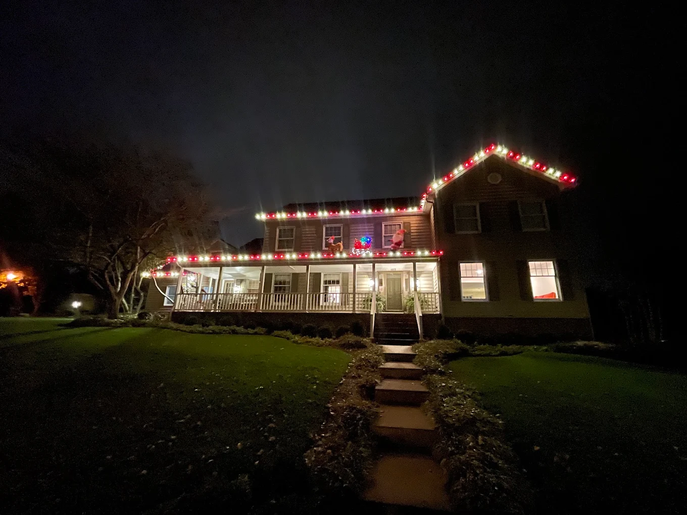 Two-story home with alternating red-and-white roofline and porch lights at night