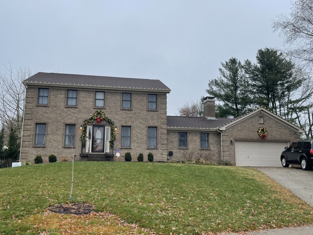 Brick colonial with roofline lights and holiday door garland, daytime