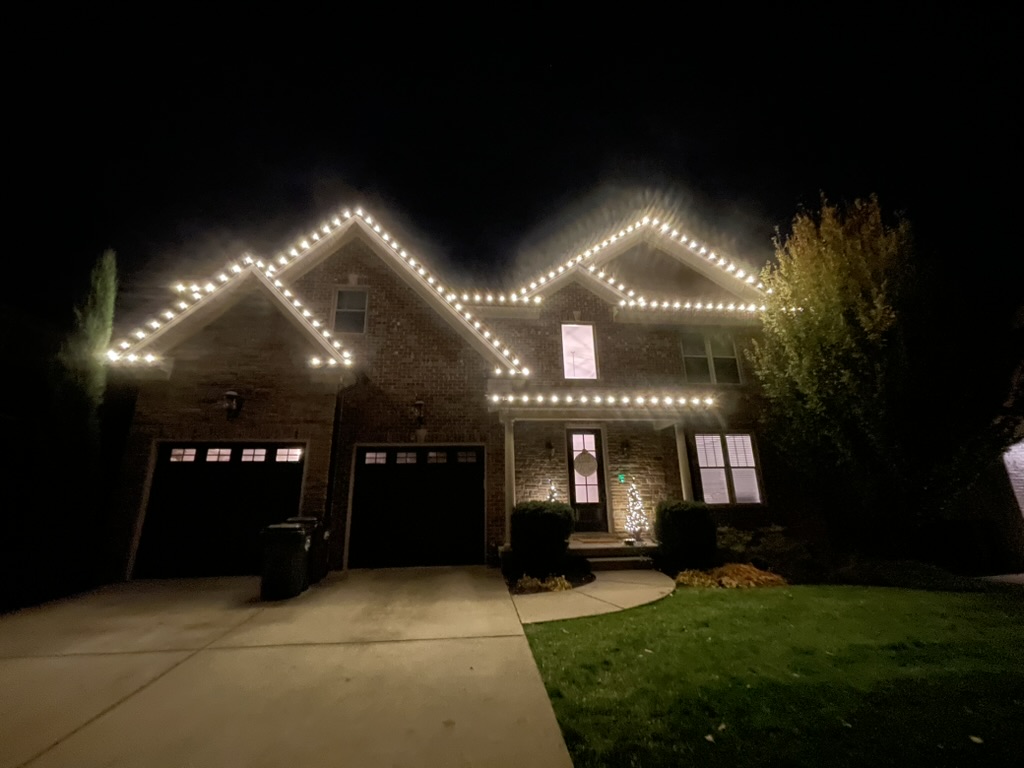 Brick two-story home with bright warm-white roofline lights at night