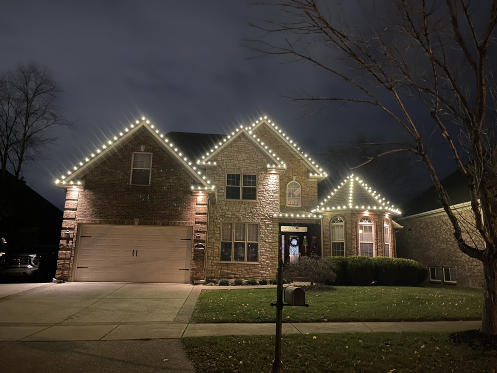 Brick two-story home with warm-white roofline lights at dusk