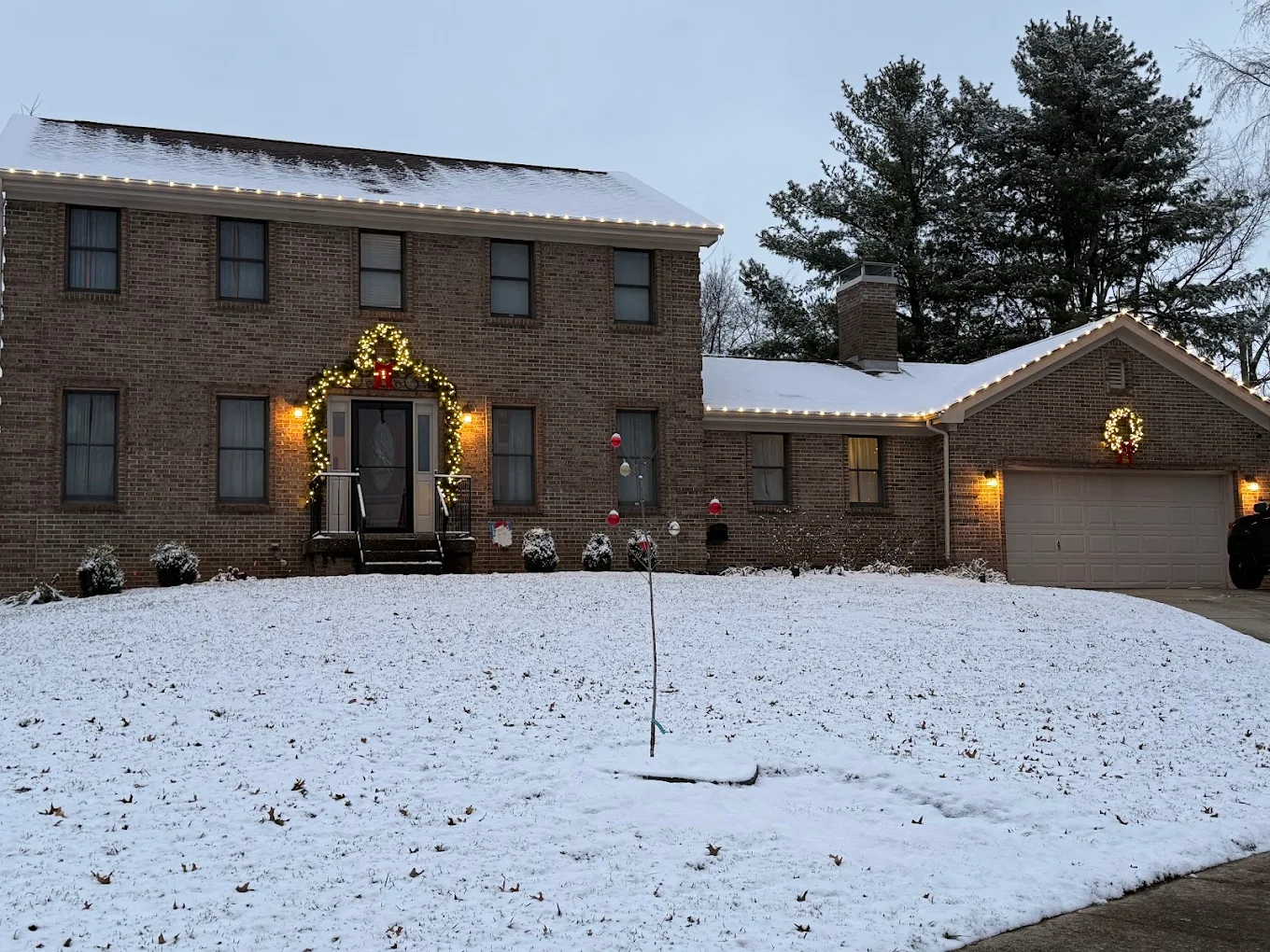 Brick colonial with roofline lights and door garland, snow on the ground