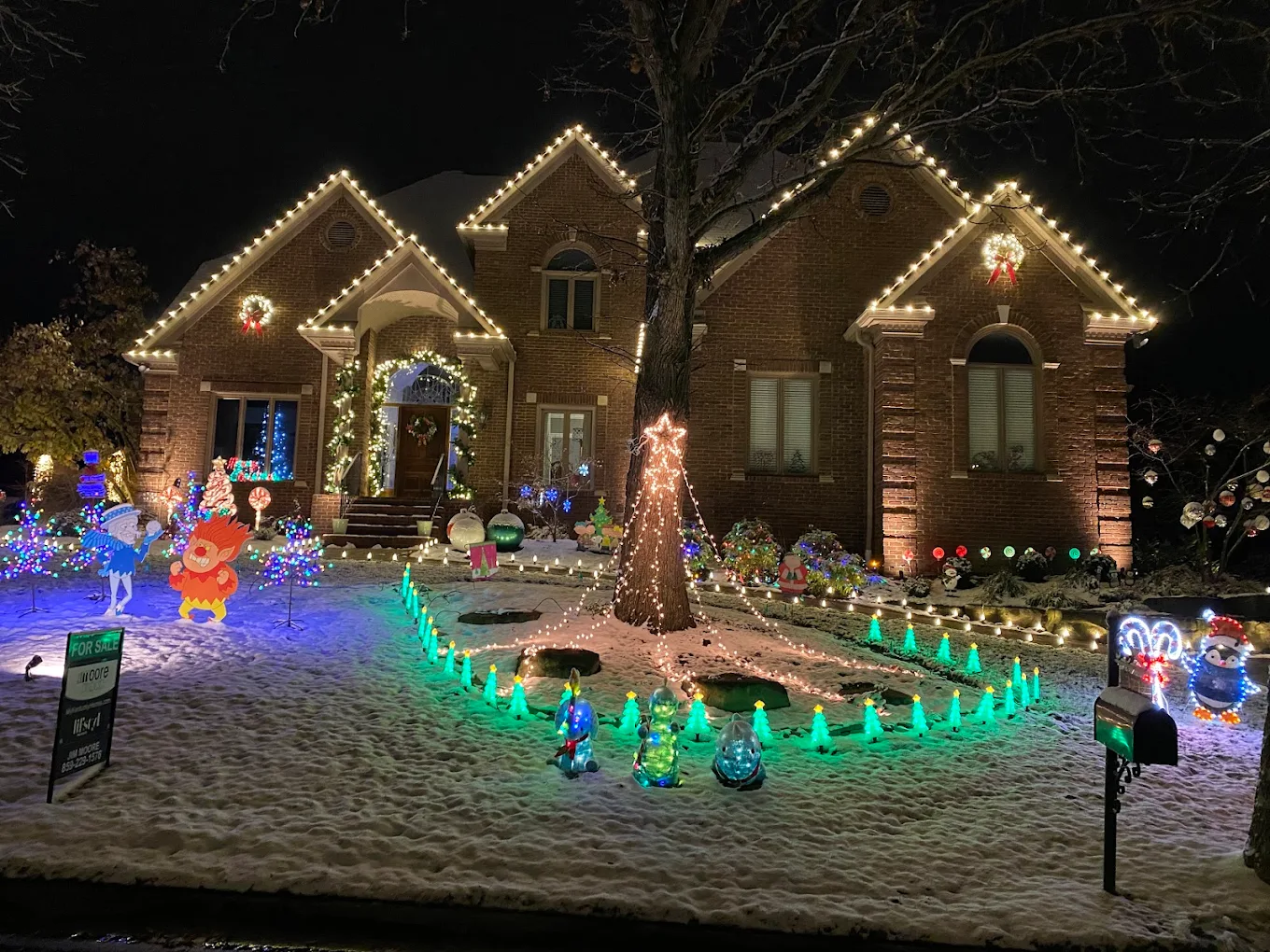 Brick home with roofline lights and a fully decorated holiday yard display at night