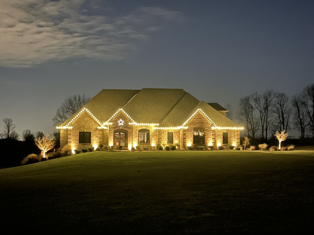 Stone ranch home with roofline lights and uplit landscaping at night