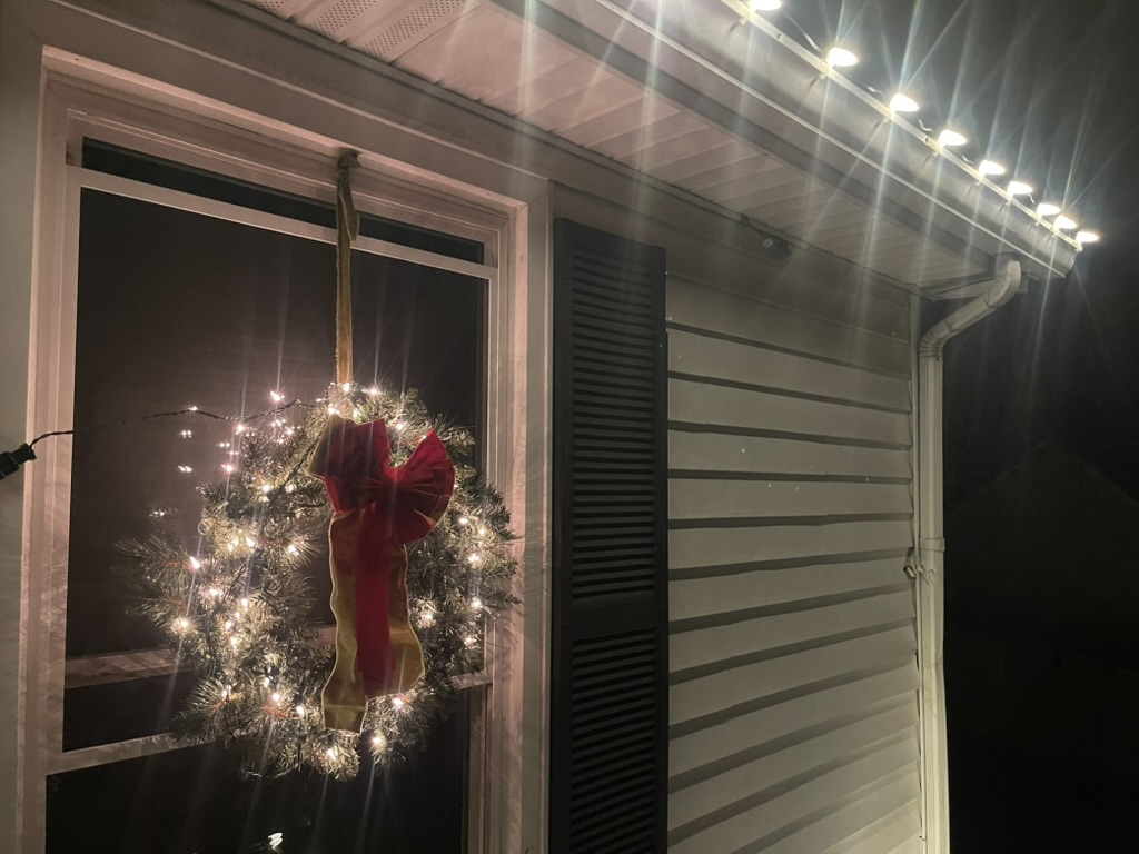 Lit wreath with a red bow beside warm-white eave lights